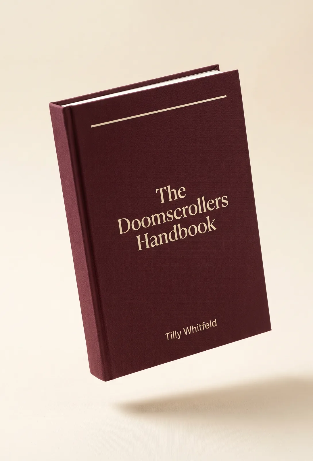 A maroon hardcover book titled The Doomscrollers Handbook, floating above a warm ivory surface